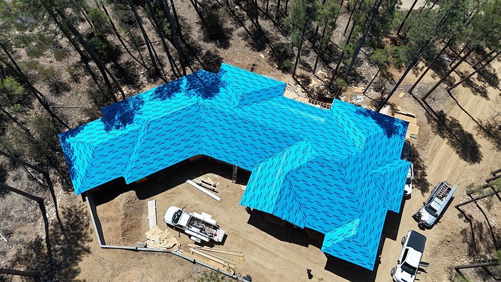 An aerial view of a house under construction with a blue tarp on the roof.