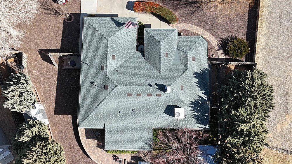 An aerial view of a large house with a green roof surrounded by trees.