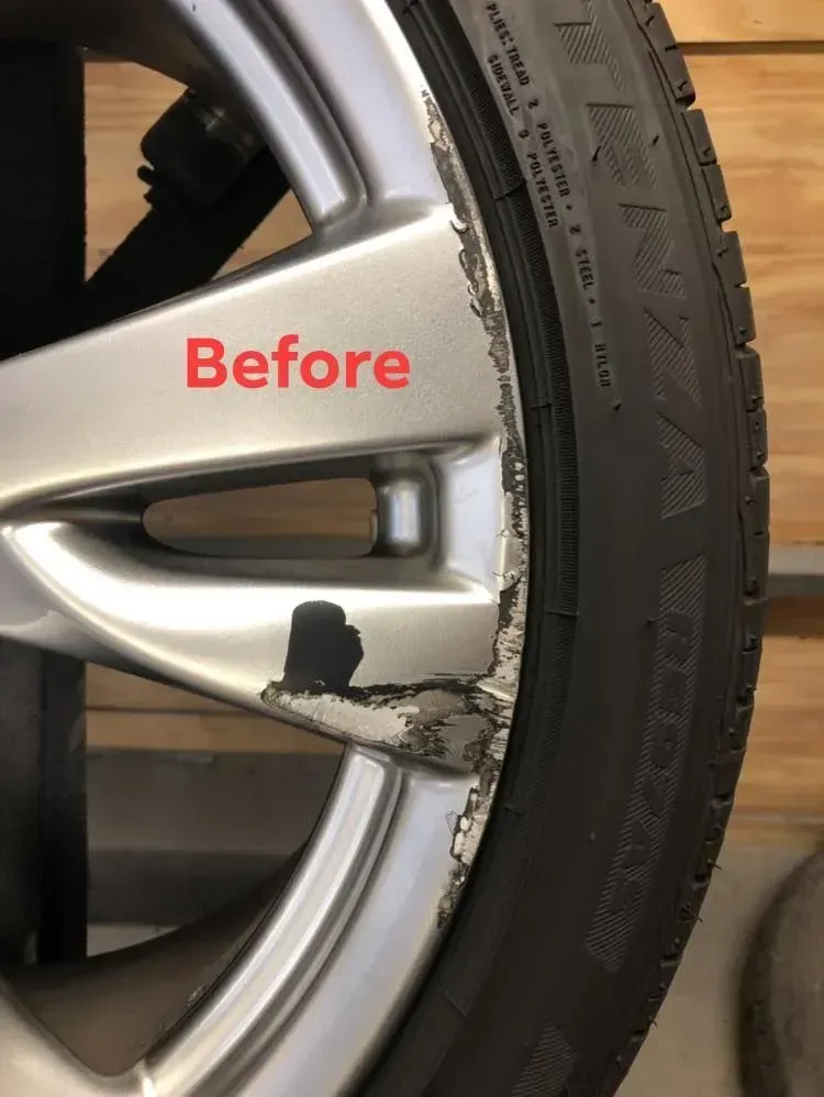 Damaged silver car wheel rim before repair, with black scuff marks near the tire