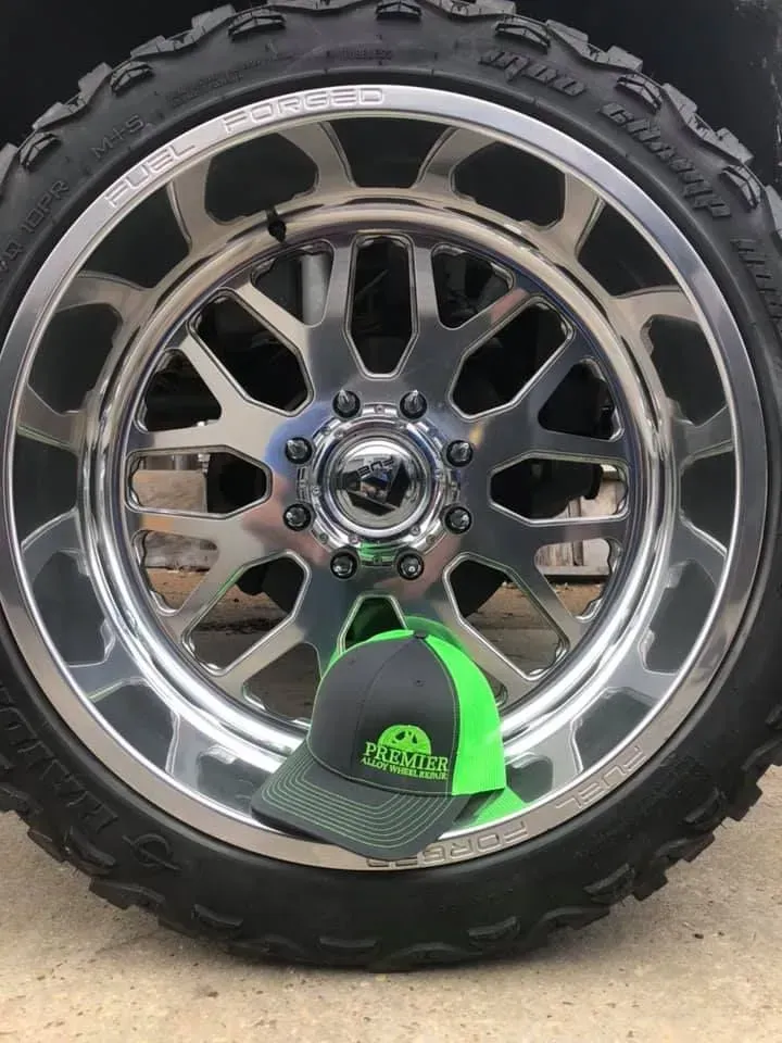 Chrome off-road wheel with black tire and neon green cap on a white background