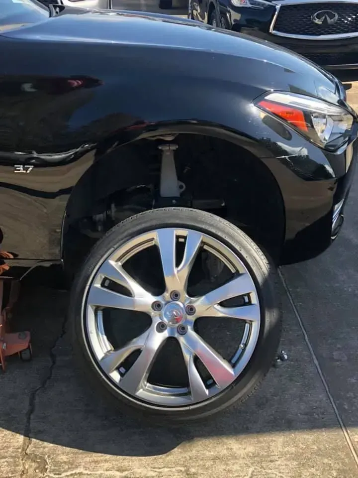 Black SUV with a silver wheel parked on a driveway, front fender missing and wheel exposed