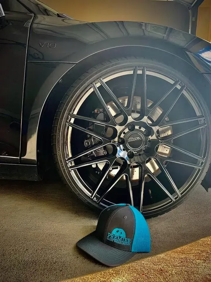 Black sports car wheel with custom rim beside a blue-and-black cap on a garage floor