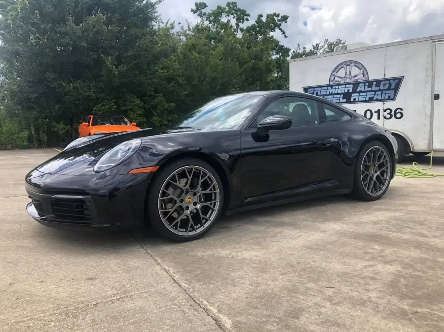 Black sports car parked on concrete near a sign and trees