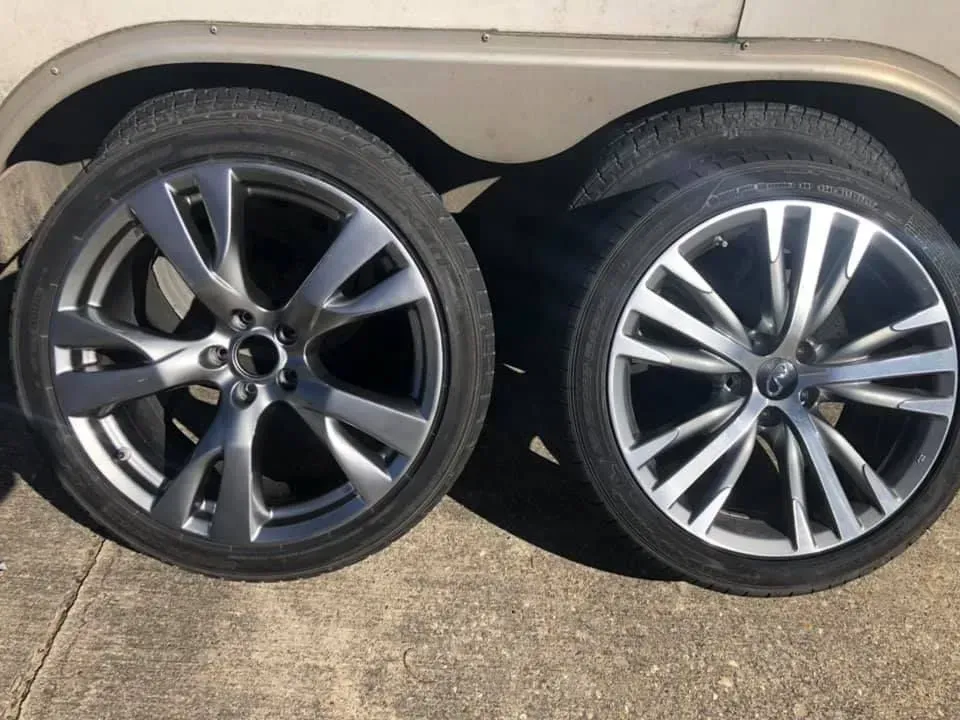Two car wheels with different alloy rim designs leaning against a beige vehicle.