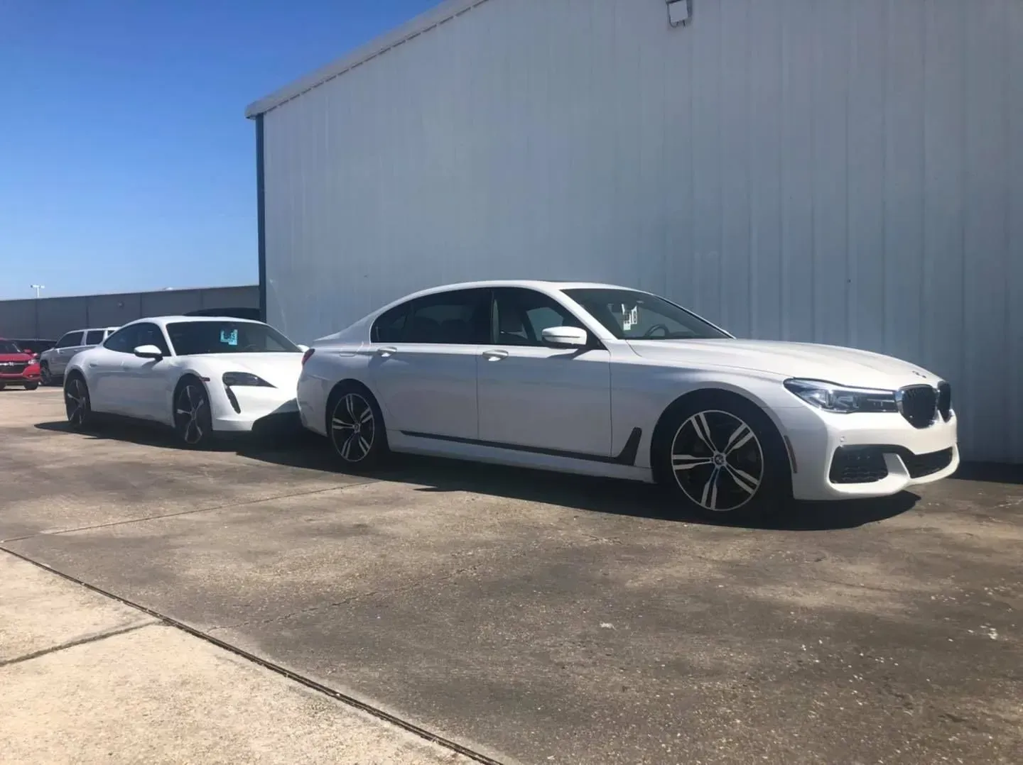 Two white sports cars parked beside a gray industrial building on a sunny day