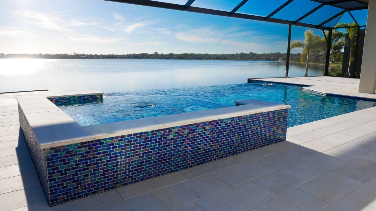 A large swimming pool with a hot tub next to it overlooking a lake.