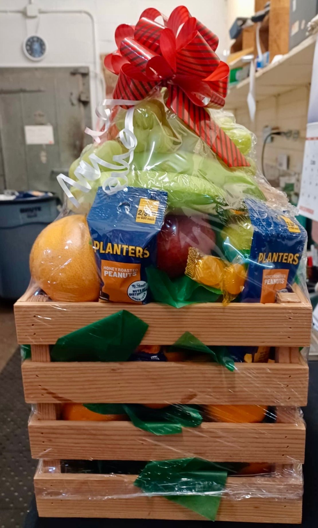 Gift basket filled with fruits, snacks, and a red bow.