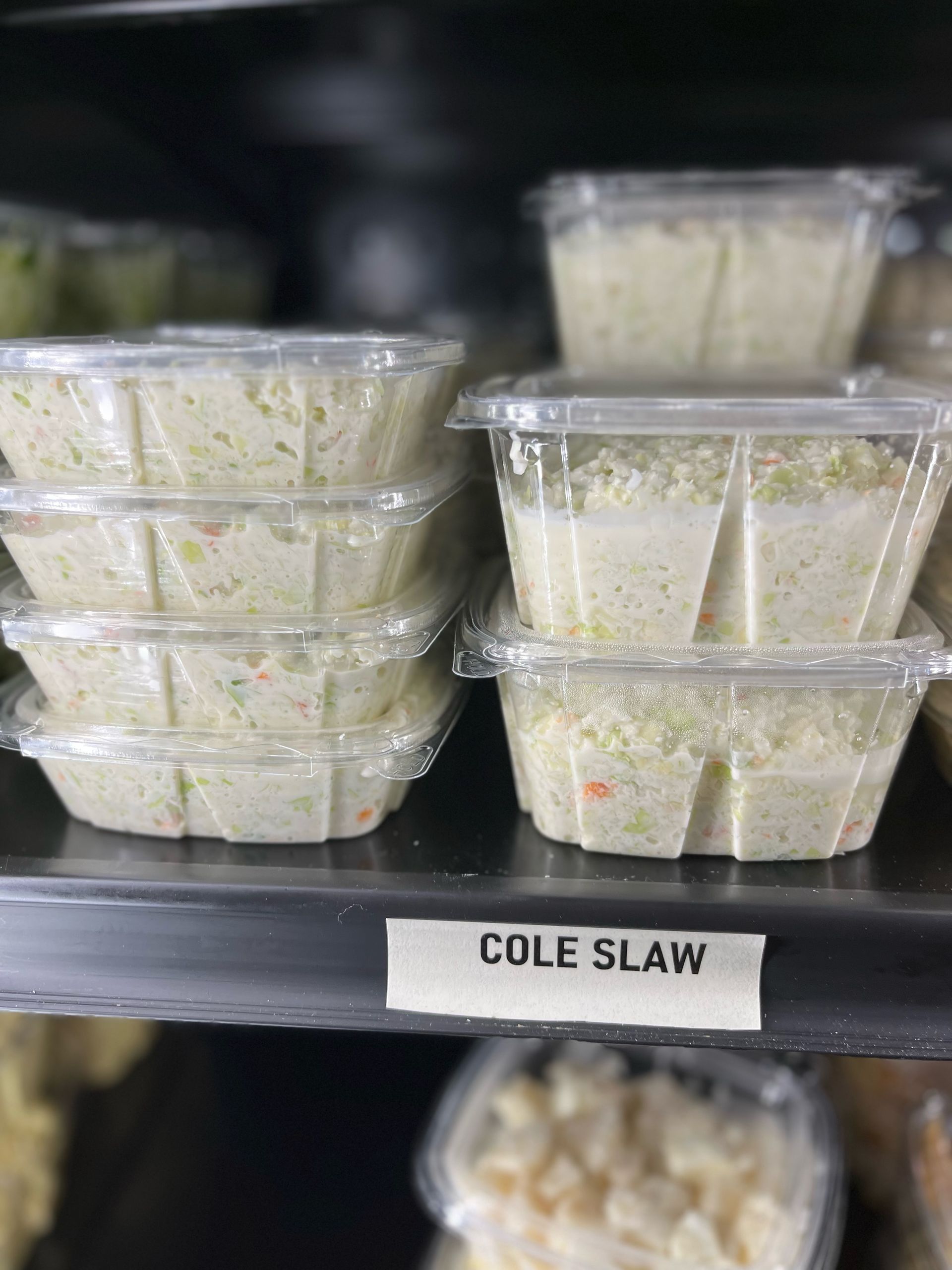 A shelf filled with plastic containers of cole slaw.