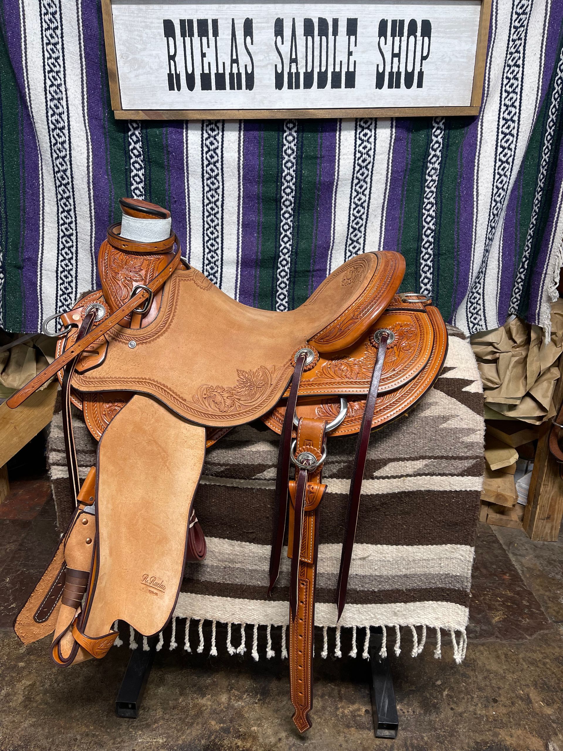 A saddle is sitting in front of a sign that says ruelas saddle shop