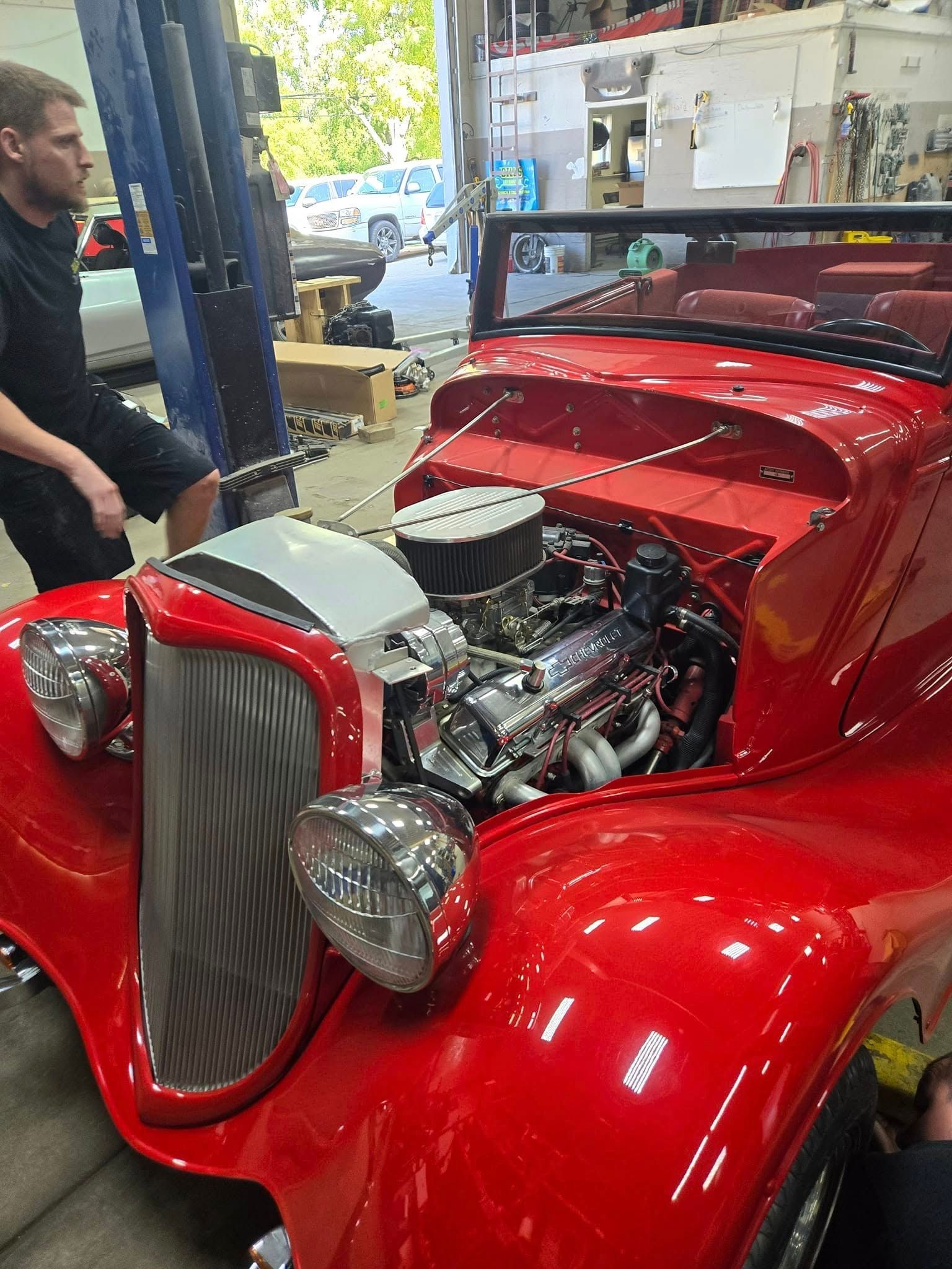 A man is working on a red car in a garage.