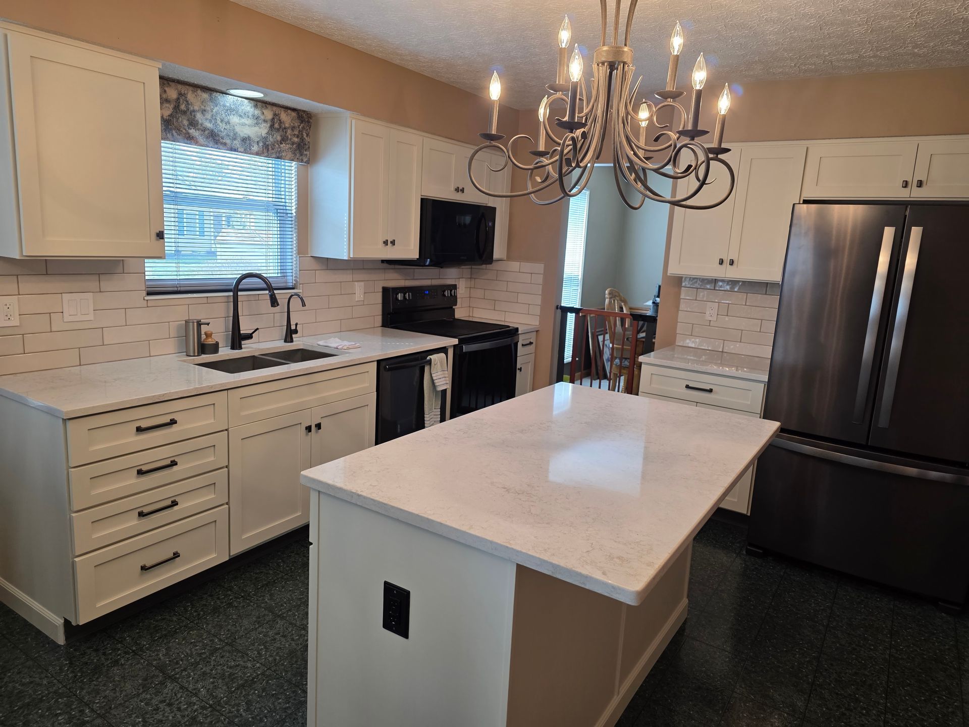 A kitchen with white cabinets , black appliances , a large island and a chandelier.