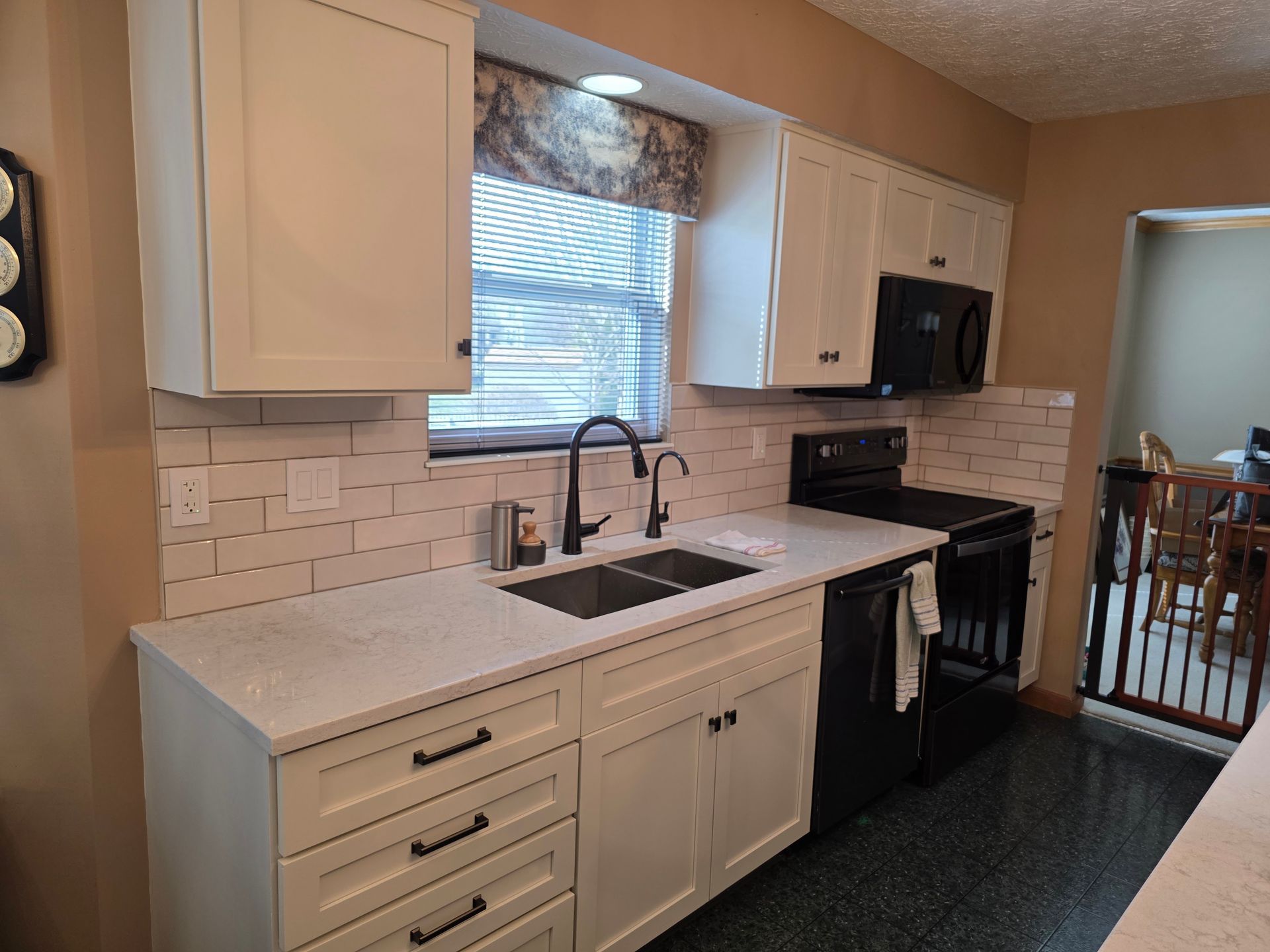 A kitchen with white cabinets , black appliances , a sink , and a window.