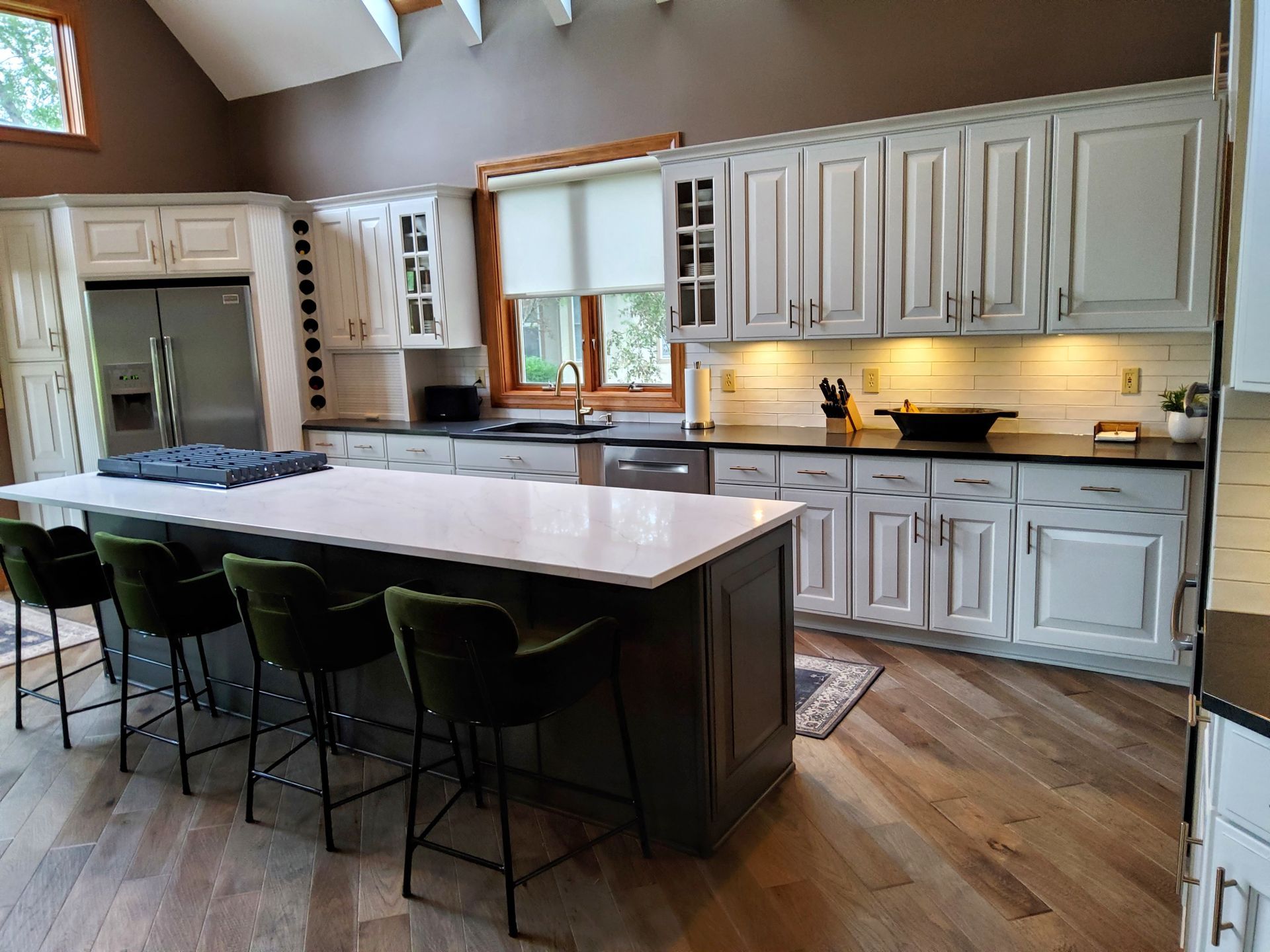 A kitchen with white cabinets , black counter tops , and a large island.