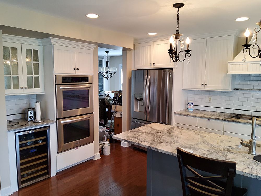 A kitchen with white cabinets , stainless steel appliances , granite counter tops and a wine cooler.
