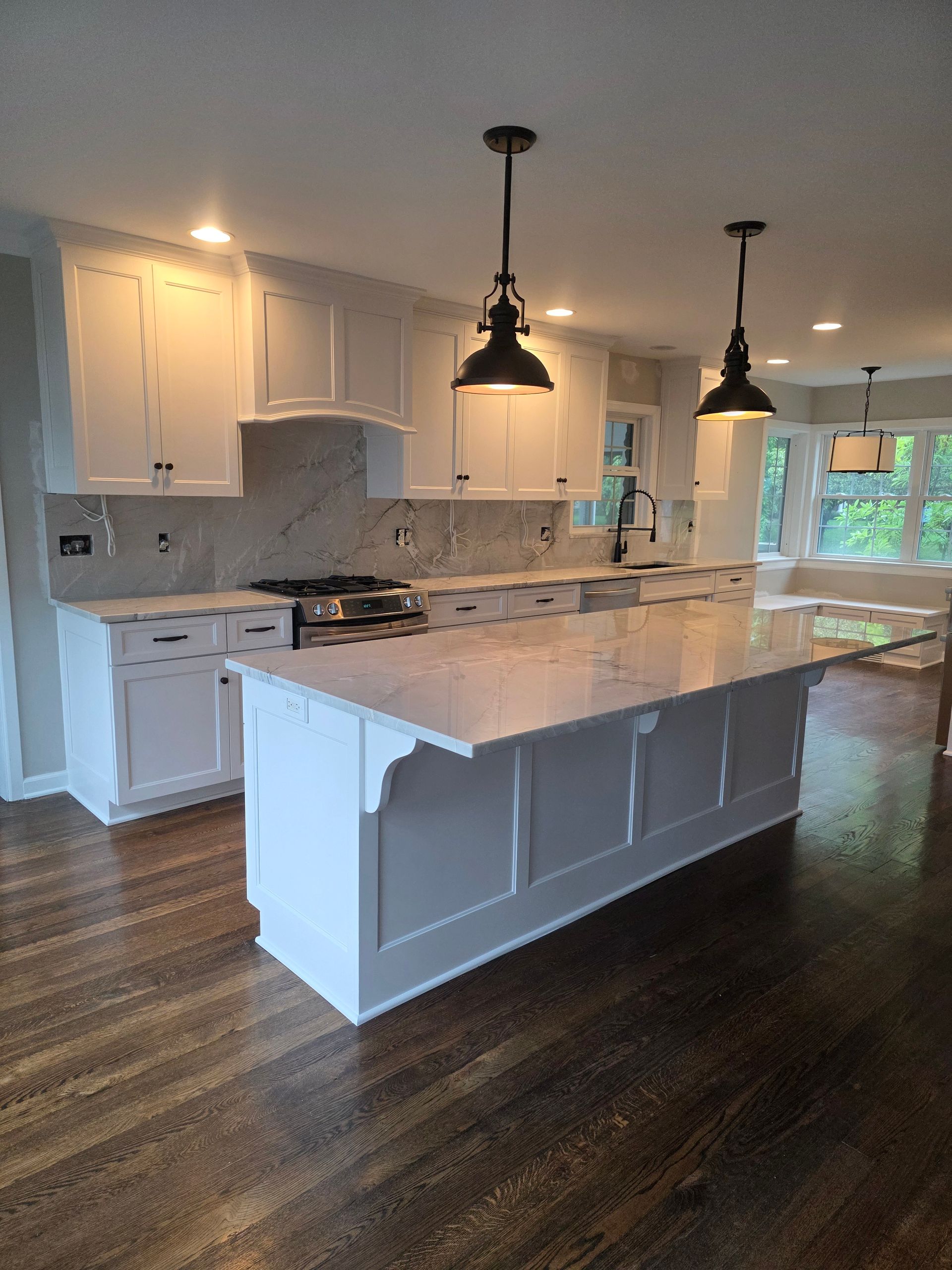 White kitchen with island, marble countertops, pendant lights, and dark wood floors.