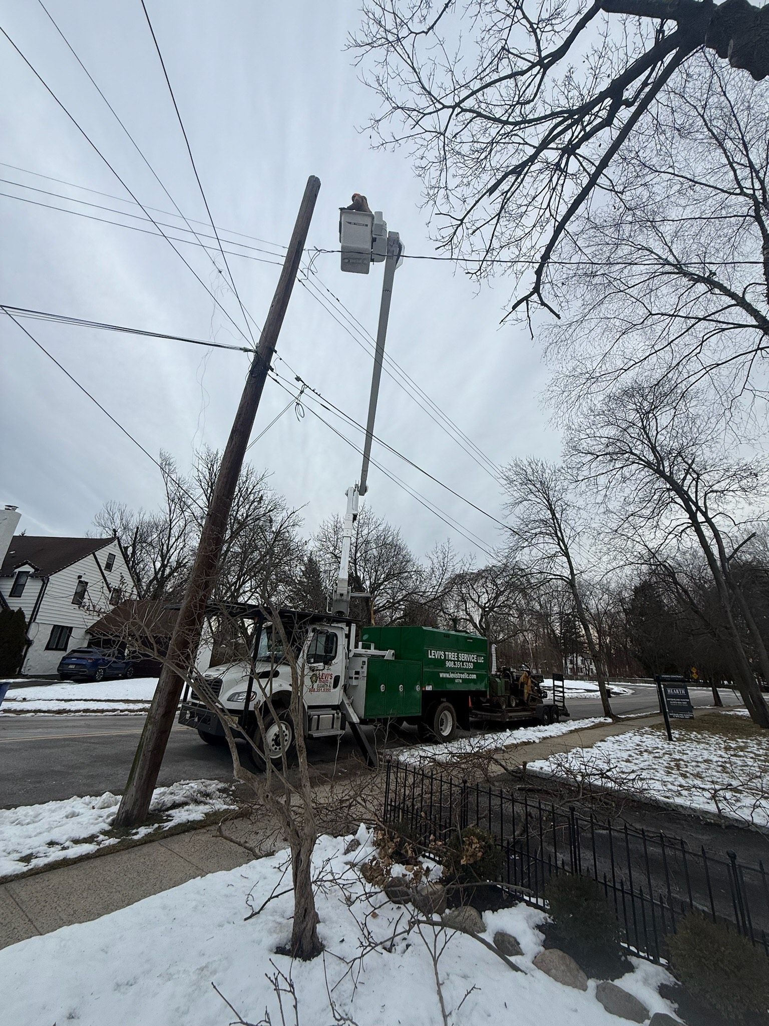 Utility truck with a lift bucket, working on power lines next to a wooden pole and trees, snow on the ground.