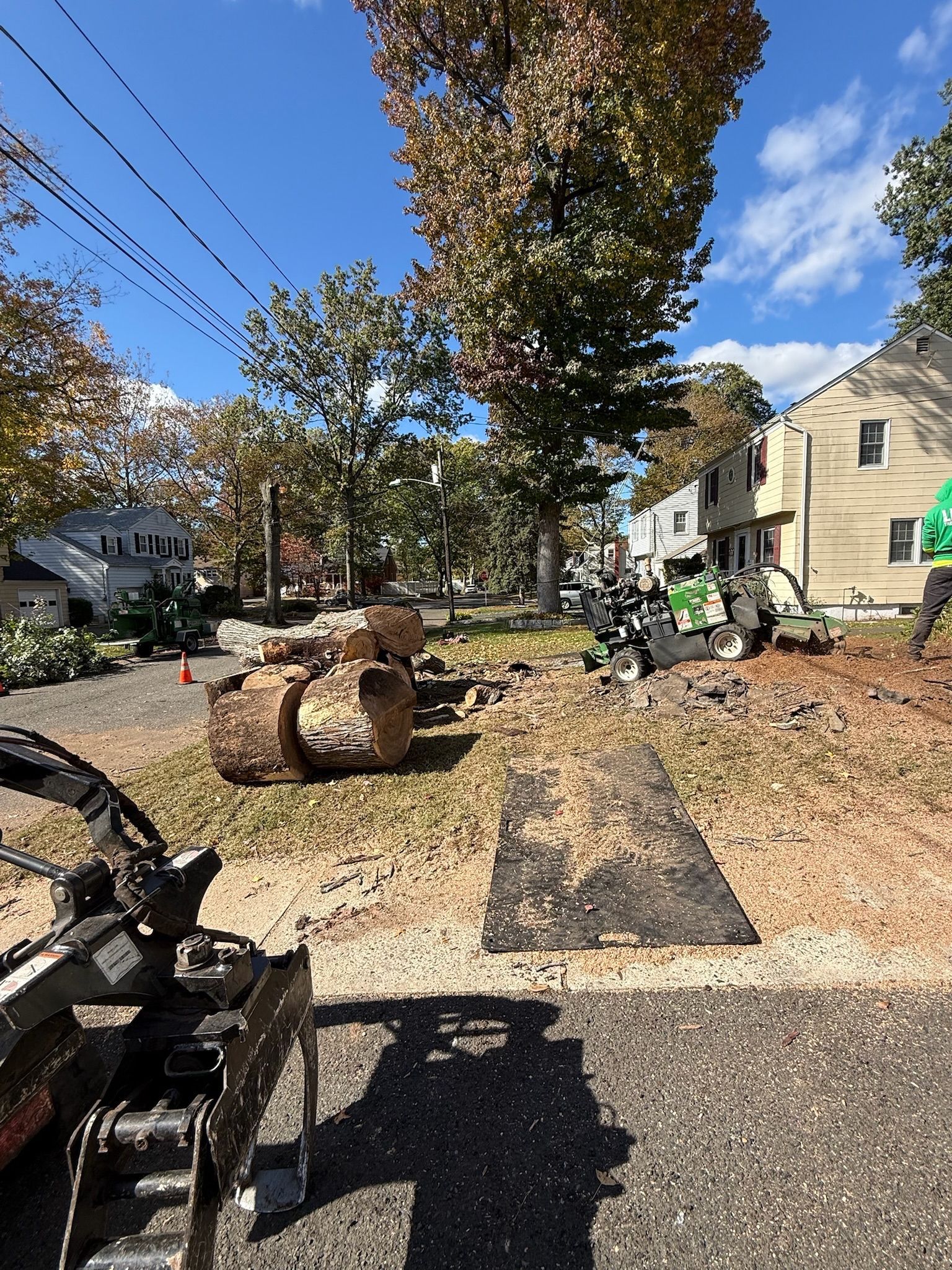Construction site with heavy machinery, trees, and houses.