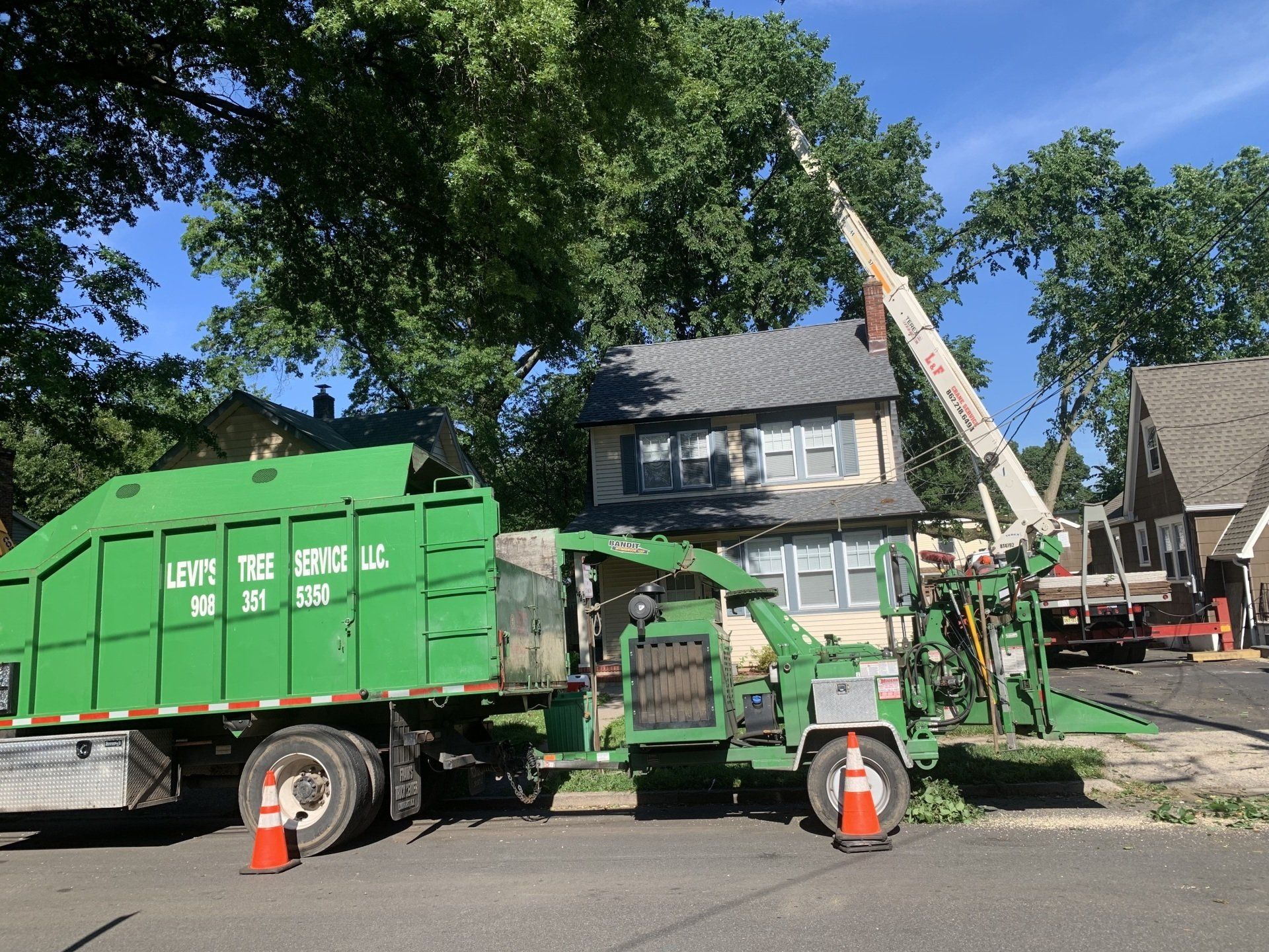 Green tree service truck with chipper trimming tree near a house.