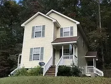 A large yellow house with a porch and stairs is surrounded by trees.