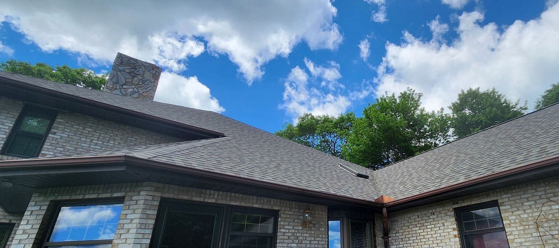 A large brick house with a gray roof and a blue sky with clouds in the background.