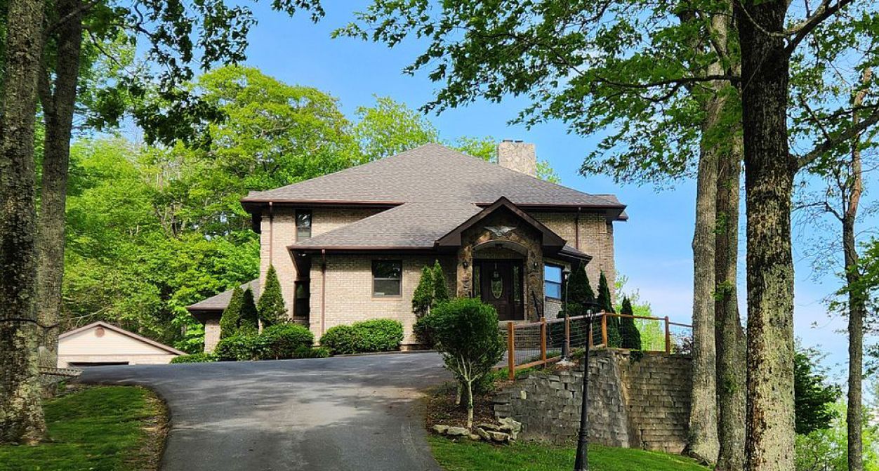 A large house with a driveway leading to it is surrounded by trees.