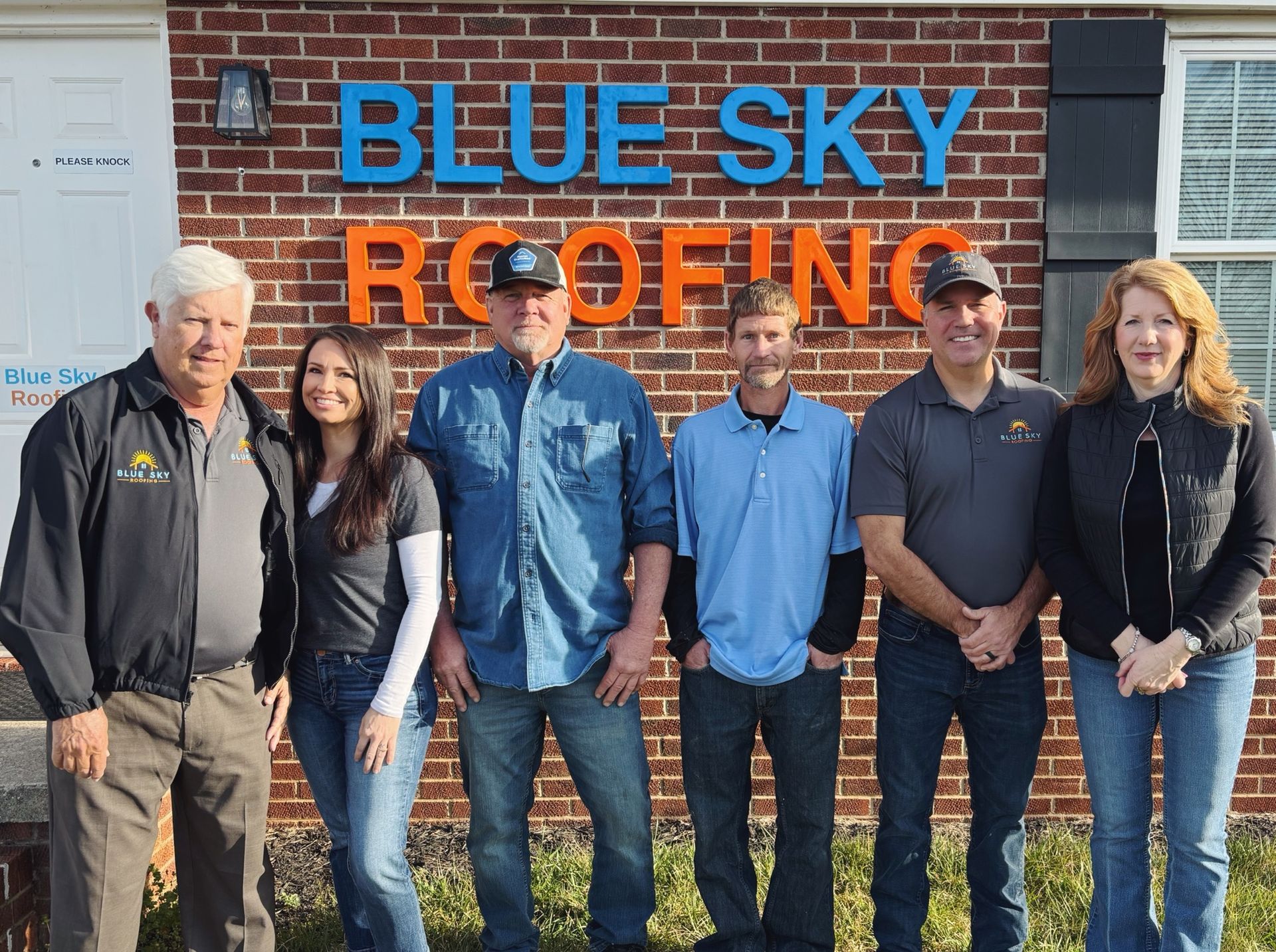 A group of people standing in front of a blue sky roofing sign
