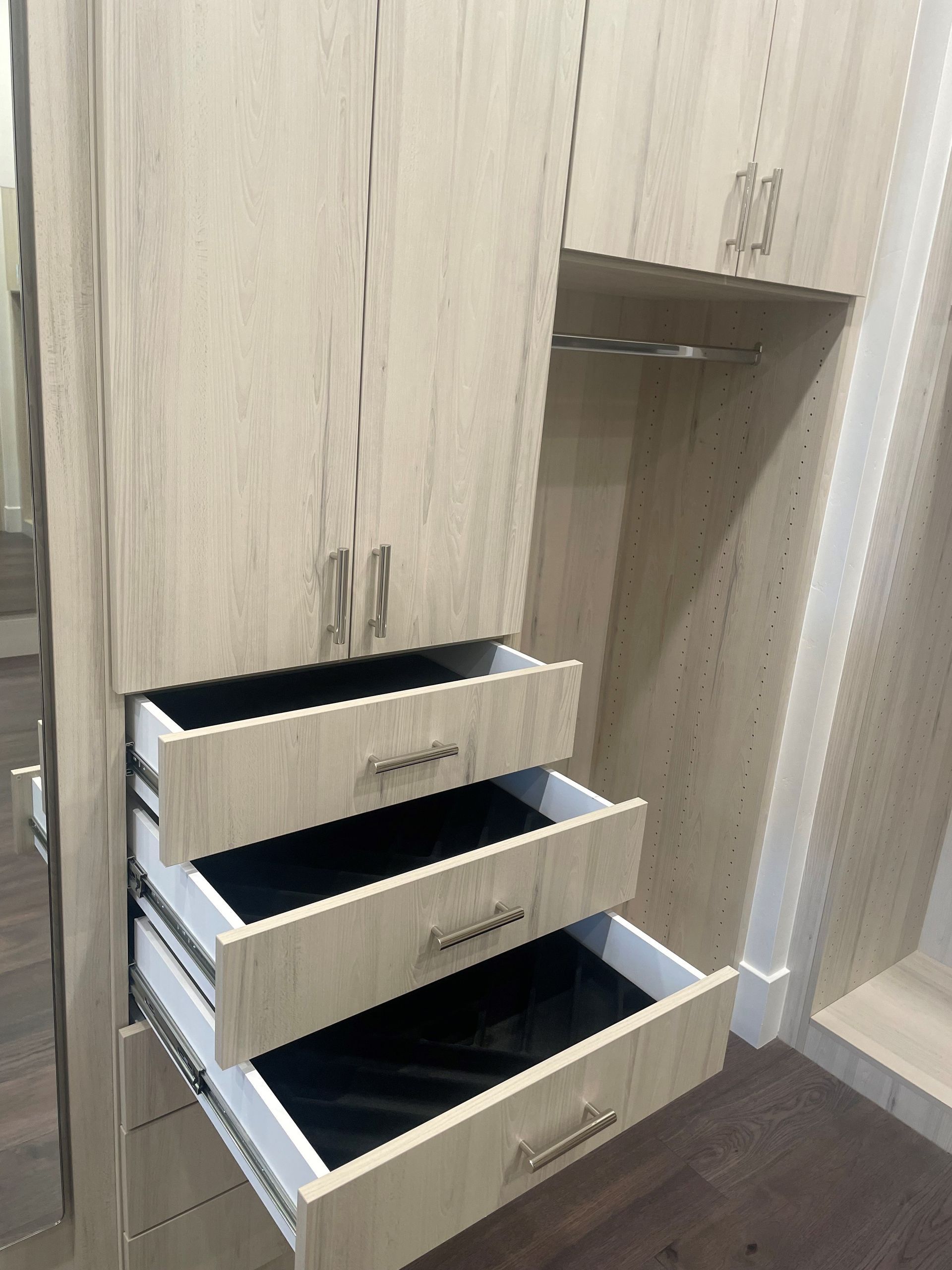 A light-colored wooden closet with three open drawers, revealing black interiors.