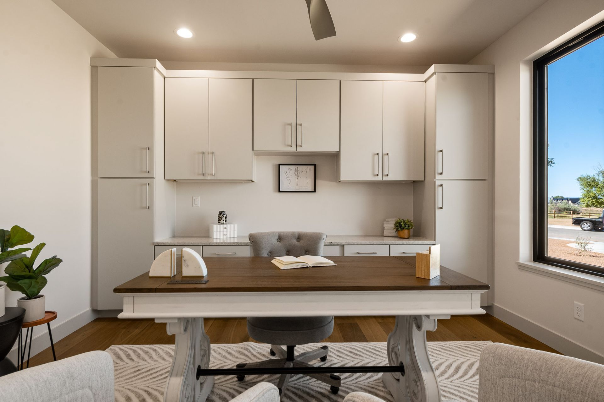 Home office with white cabinets, a wood desk, and a window overlooking a desert landscape.