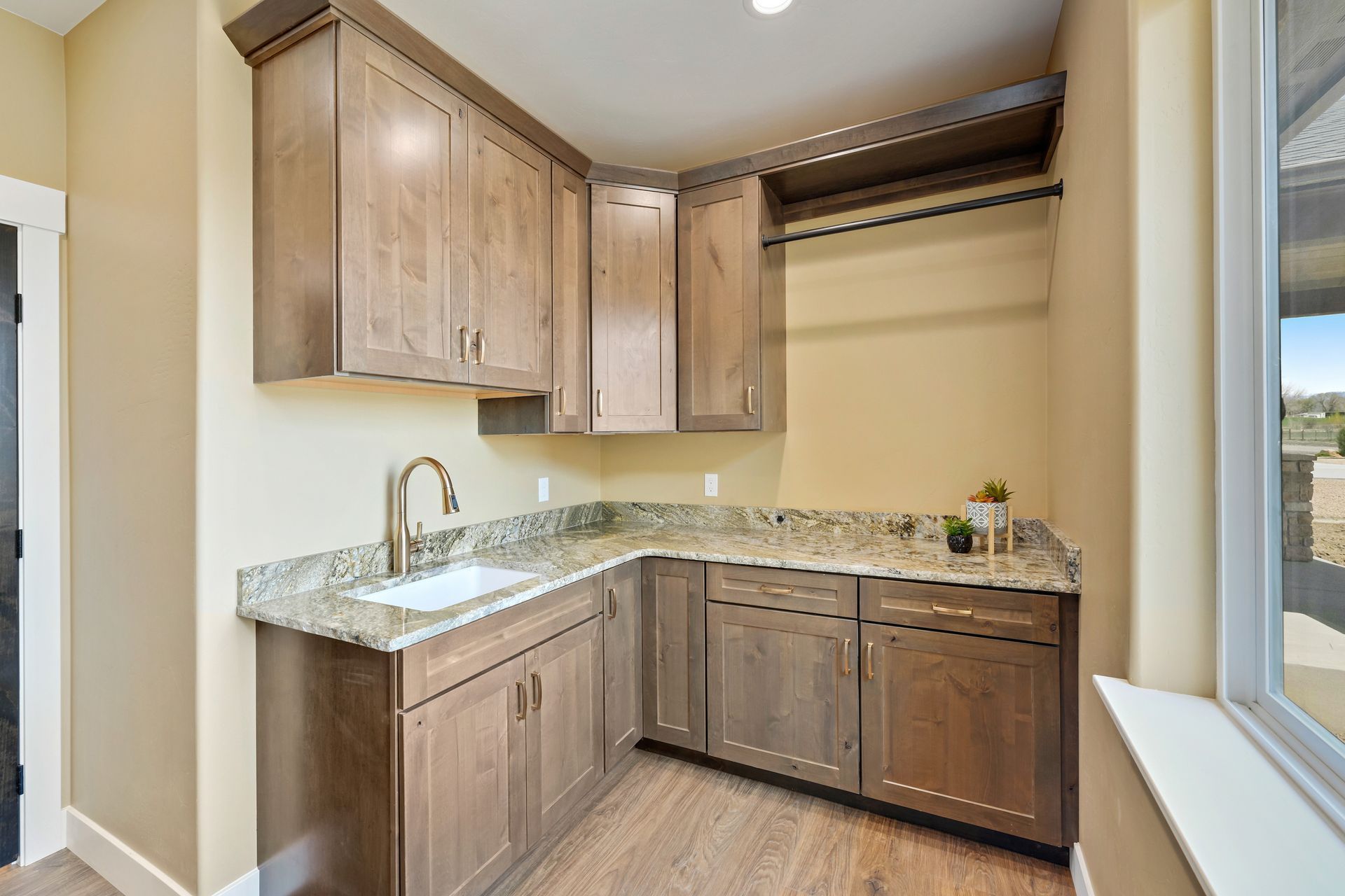 A laundry room with wooden cabinets, granite counter tops, and a sink