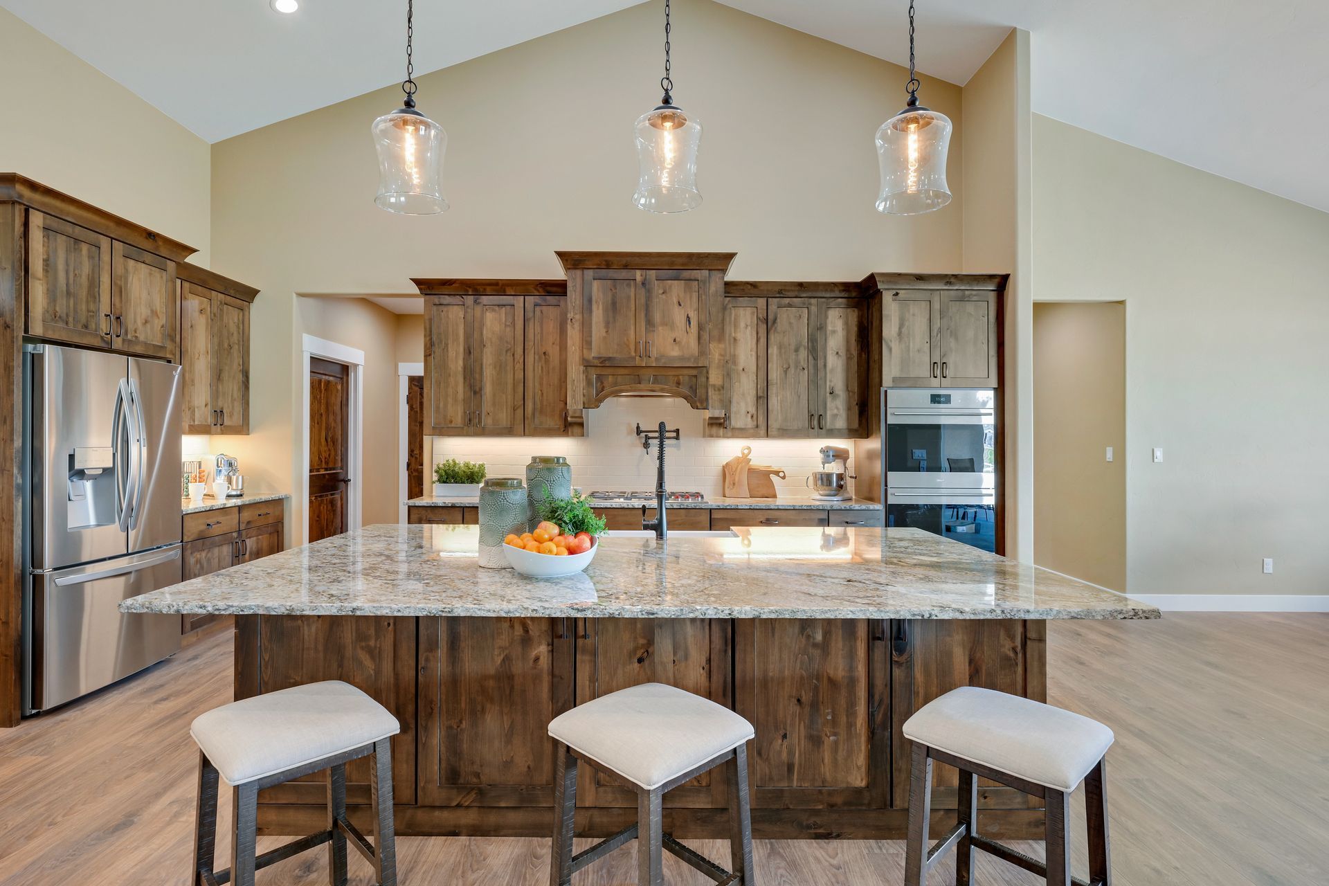 A kitchen with wooden cabinets, granite counter tops, stools, and a large island