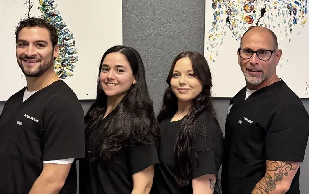Four people in black scrubs smiling, standing in front of two abstract paintings.