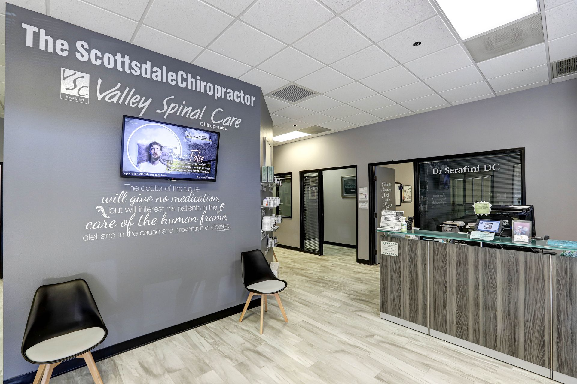 Reception area of The Scottsdale Chiropractor with gray walls, TV, chairs, and desk.