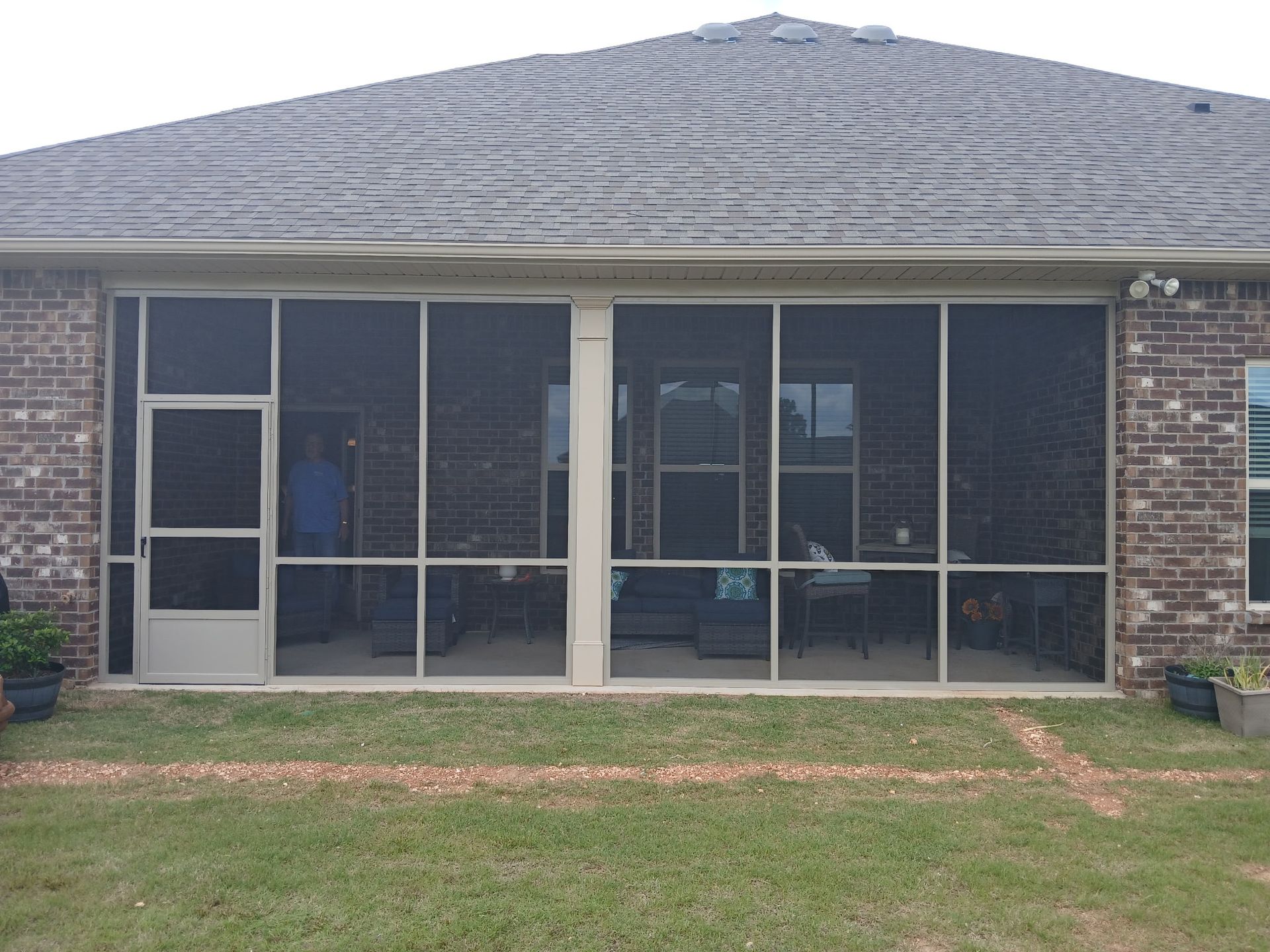 Screened porch on a brick house with white supports and a gray shingled roof