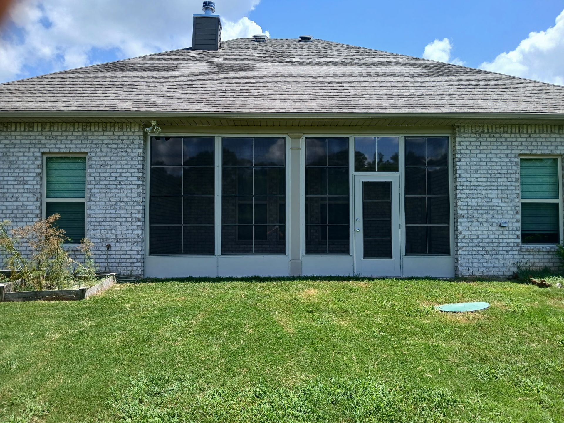 Backyard view of a single-story house with white brick, large windows, a glass door, and green lawn