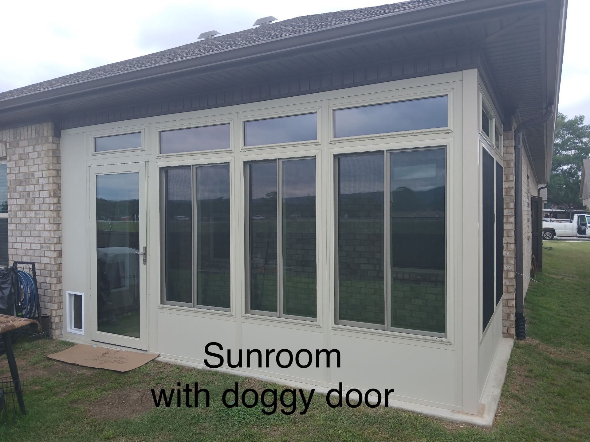 Sunroom with white-framed windows and a doggy door on a gray house exterior