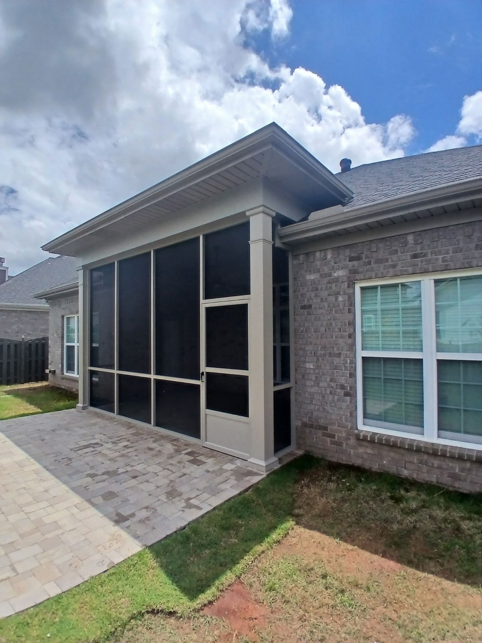 Screened patio beside a brick house with a paved walkway and cloudy sky