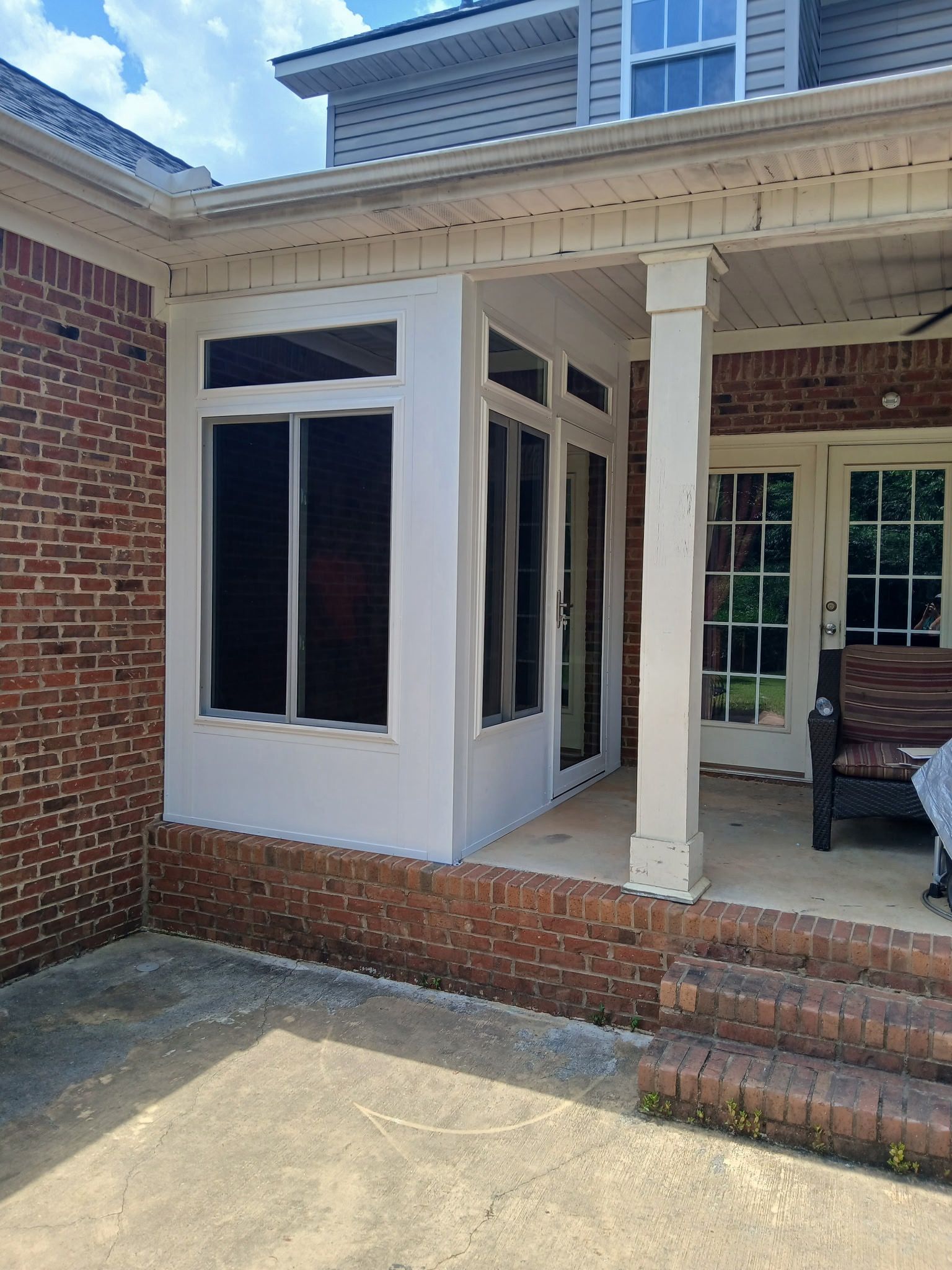 Brick house porch with a white enclosed sunroom and brick steps leading to a covered entry
