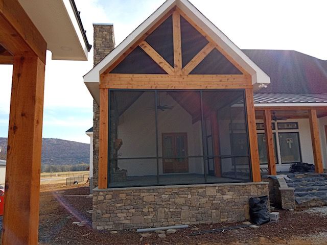 Front porch with screened enclosure, wood trim, stone base, and mountain view behind the house