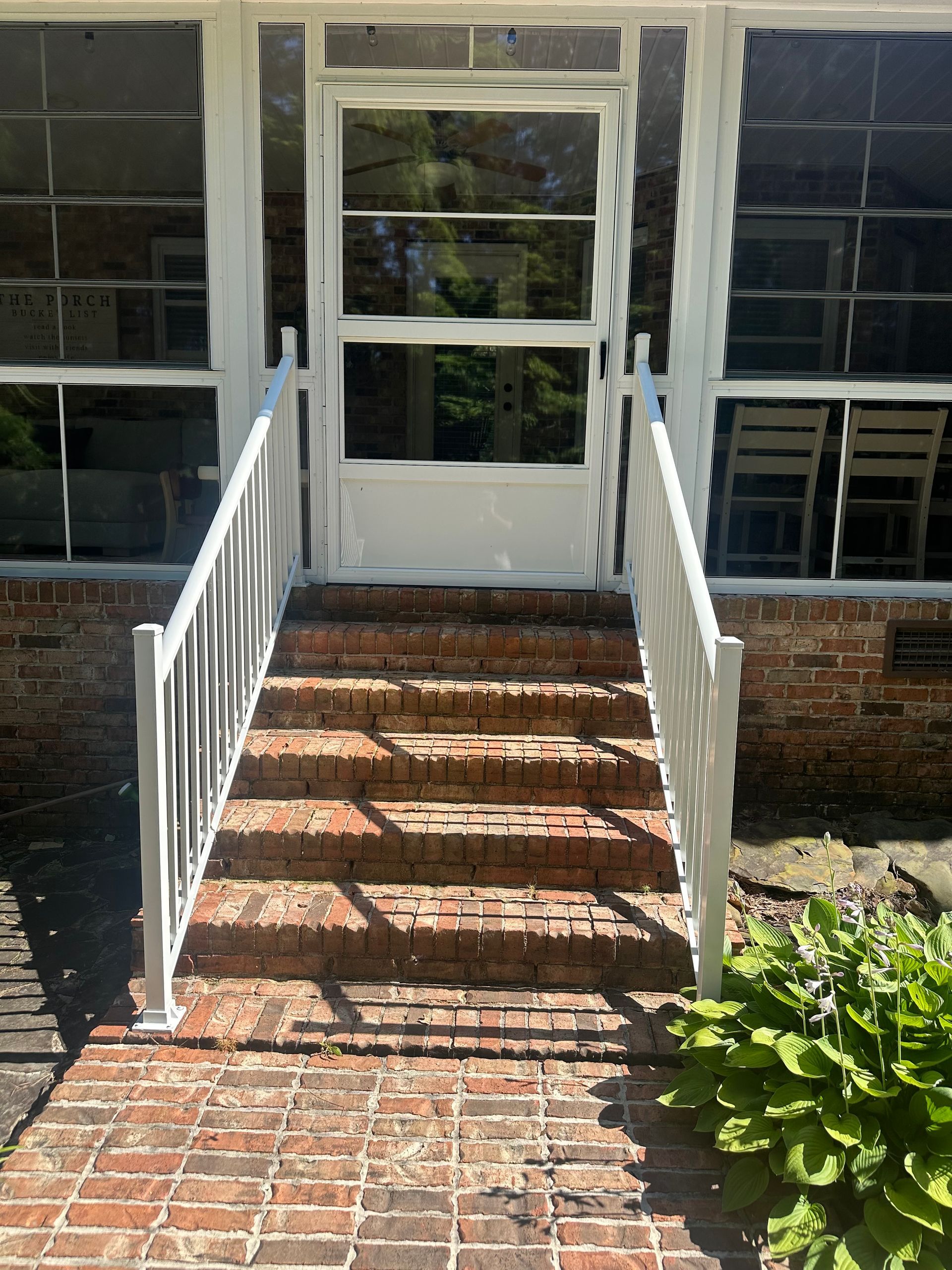 Brick steps with white railings leading to a white door on a house porch.