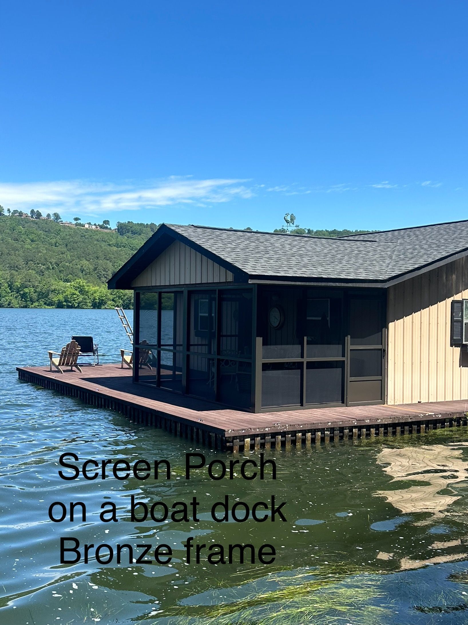 Screen porch on a boat dock with bronze frame beside blue water and wooded shoreline