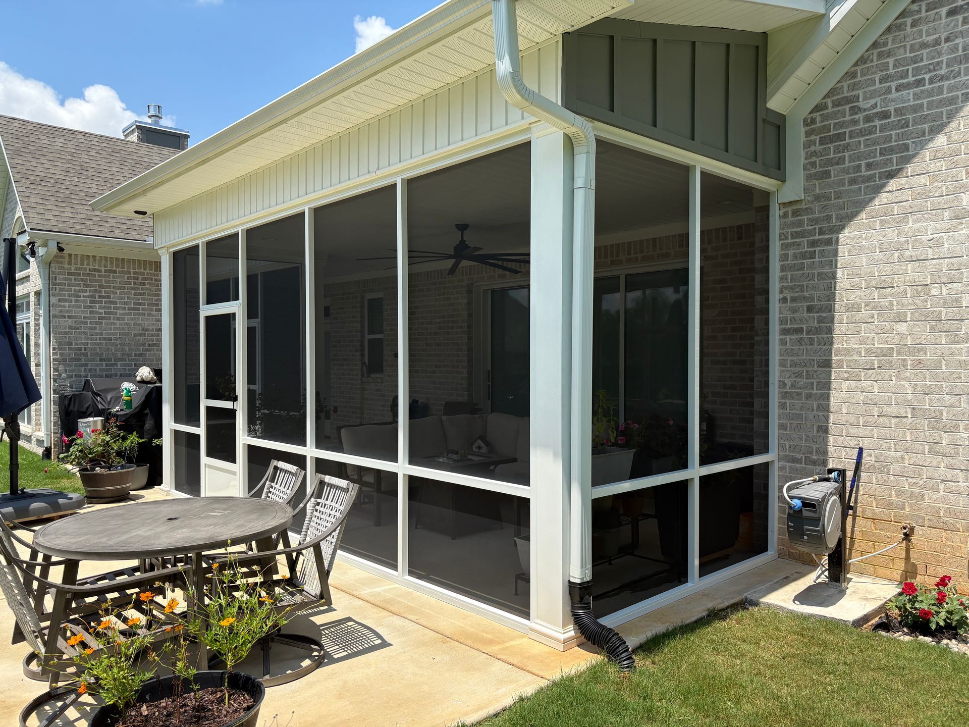 Screened-in patio with white-framed windows, brick house exterior, and outdoor furniture on a sunny day