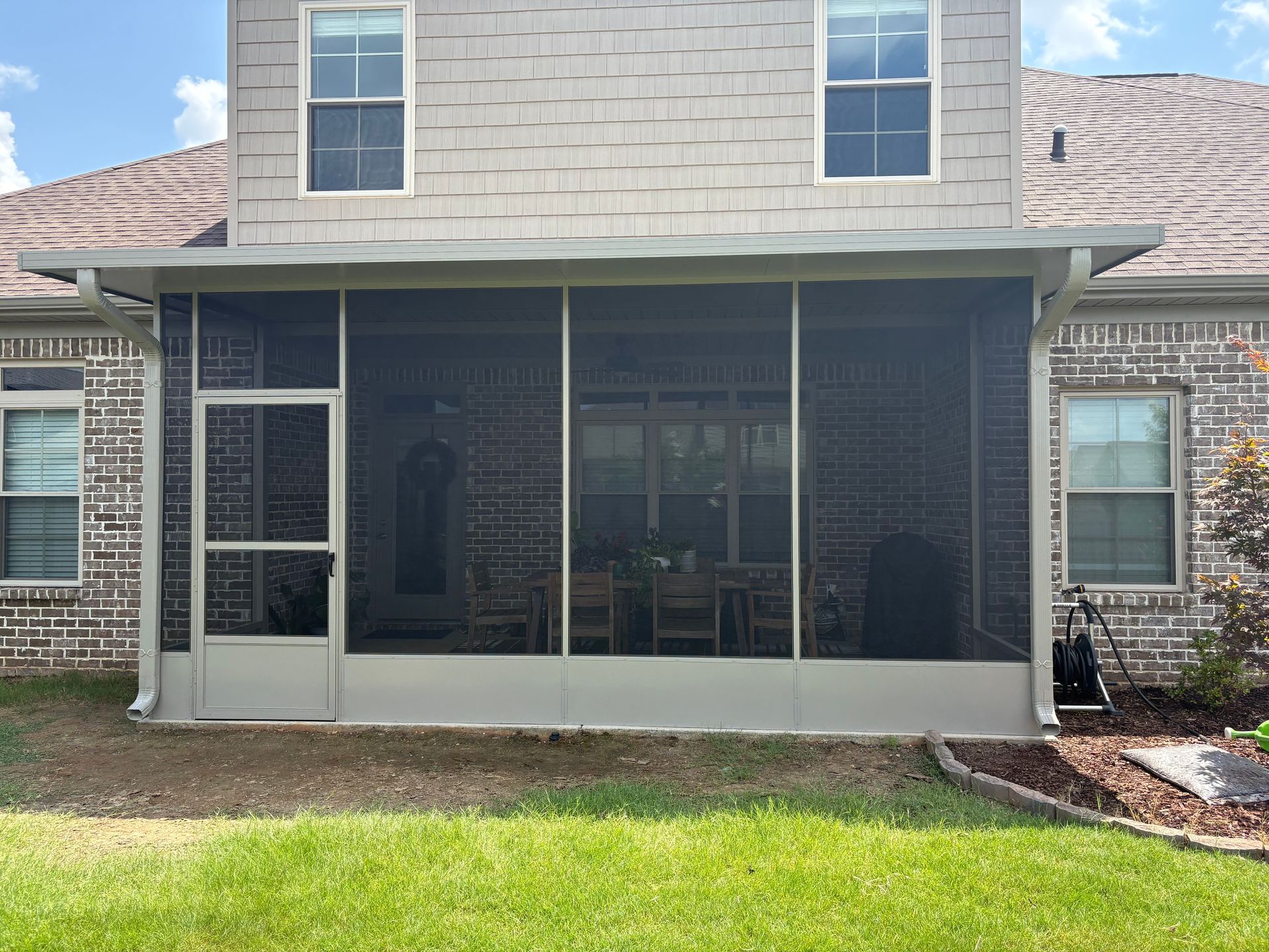 Screened back porch on a brick house with a sliding door, windows, and a small lawn in front.