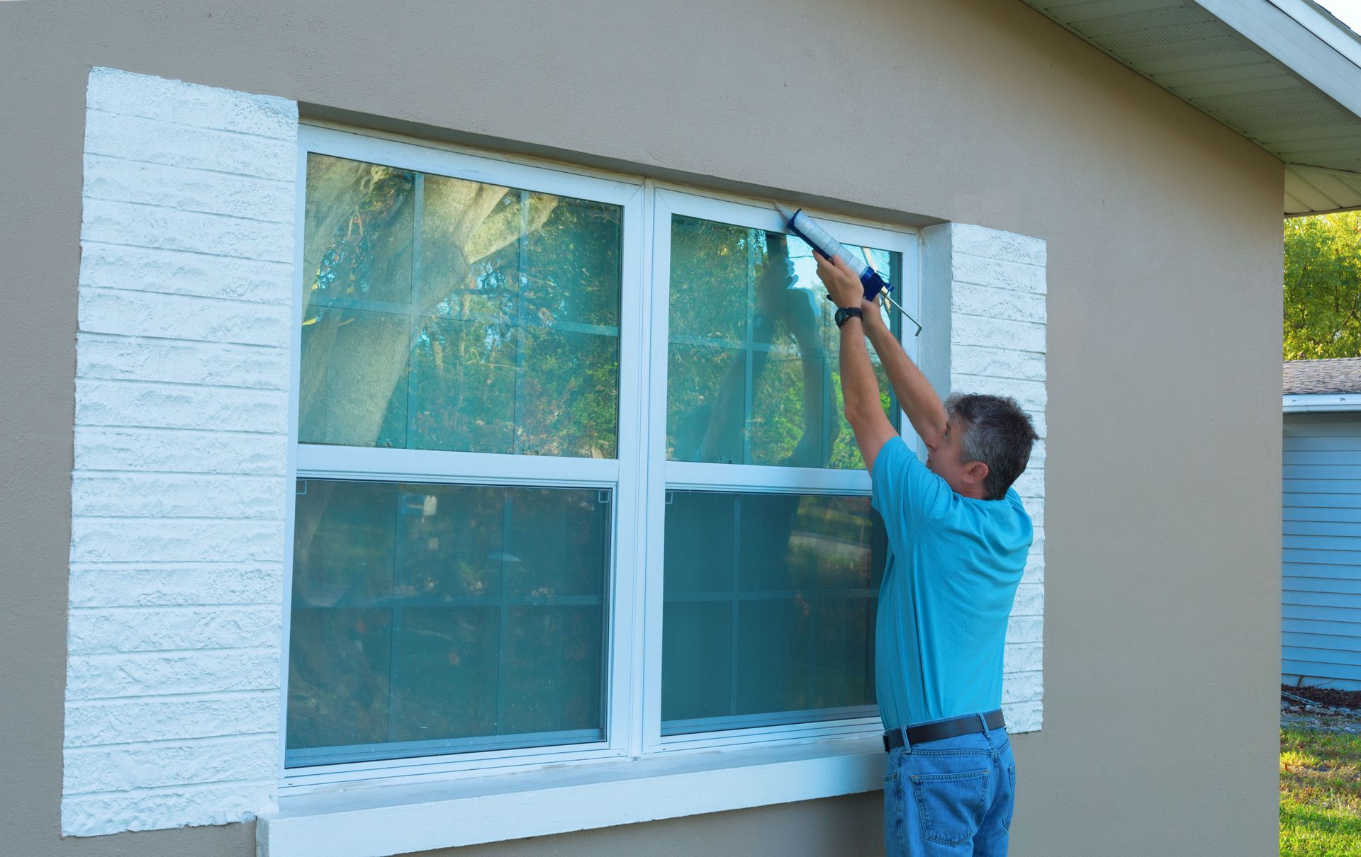 Worker painting the top corner of a house window with blue trim