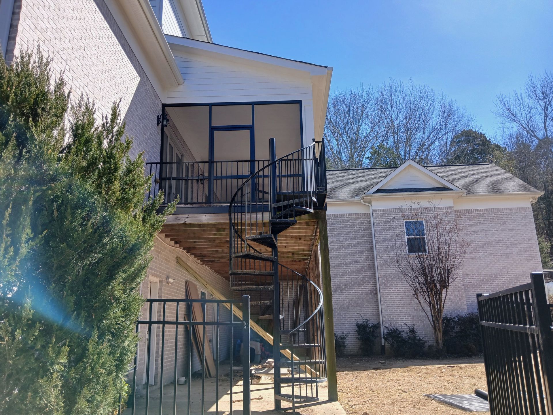Outdoor apartment staircases and balconies beside a house, with black railings and a tree in front.