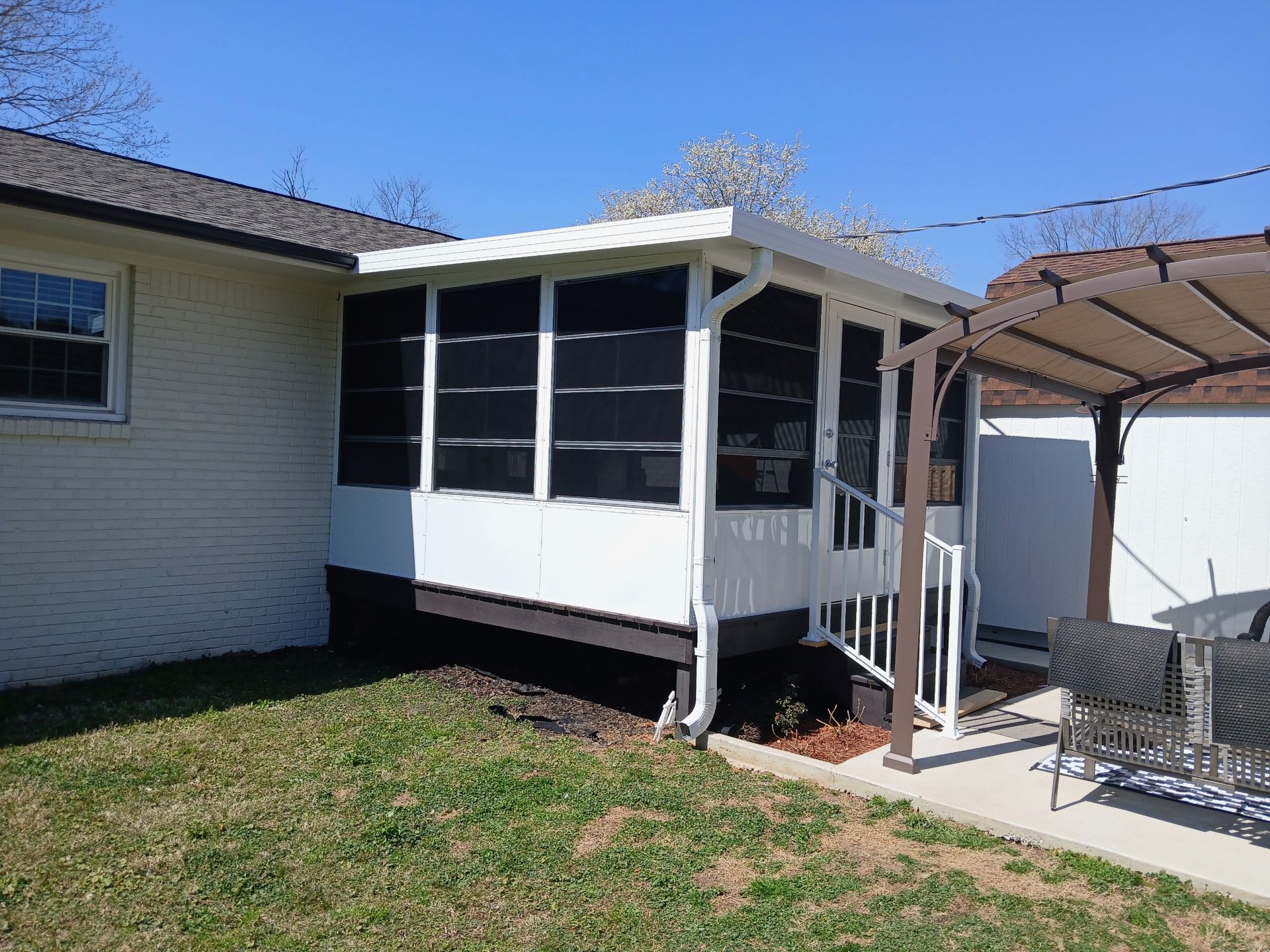 Small white screened porch attached to a house beside a covered patio and fenced yard.