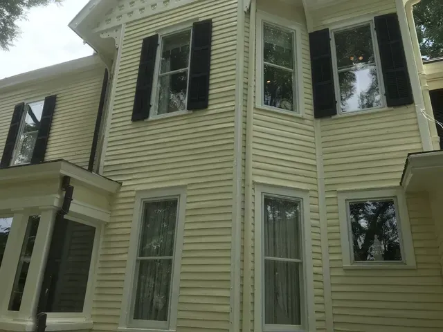 Two-story yellow house with black shutters and white-trimmed windows viewed from below
