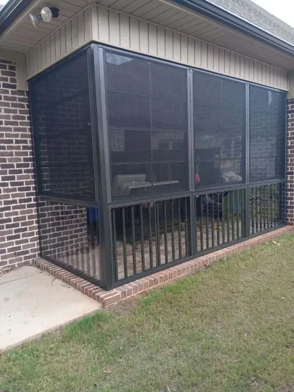 Screened patio enclosure with black metal framing beside a brick house and lawn