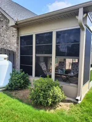 Screened patio with large windows, brick wall, and small shrubs beside a green lawn