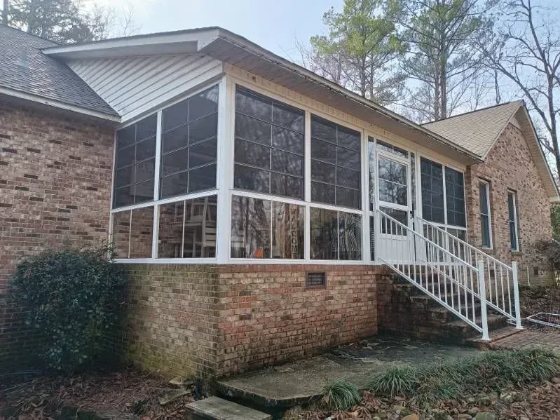 Brick house with a screened porch and white stairs on a wooded lot
