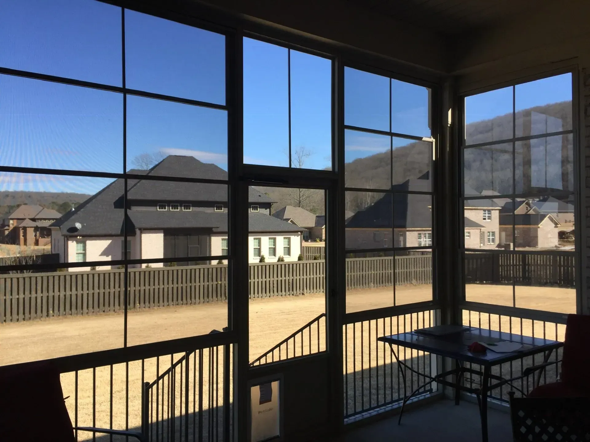 Covered patio overlooking houses and mountains through large windows, with a small table and chairs.